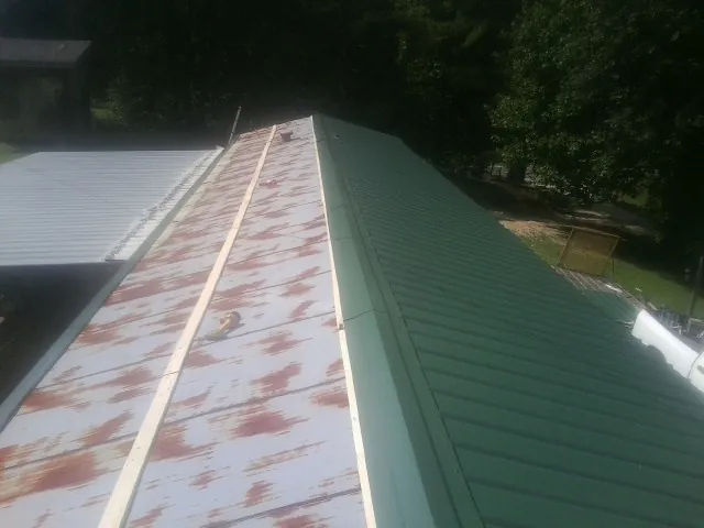 Old rusted panels beside newly installed green metal roofing in Autaugaville
