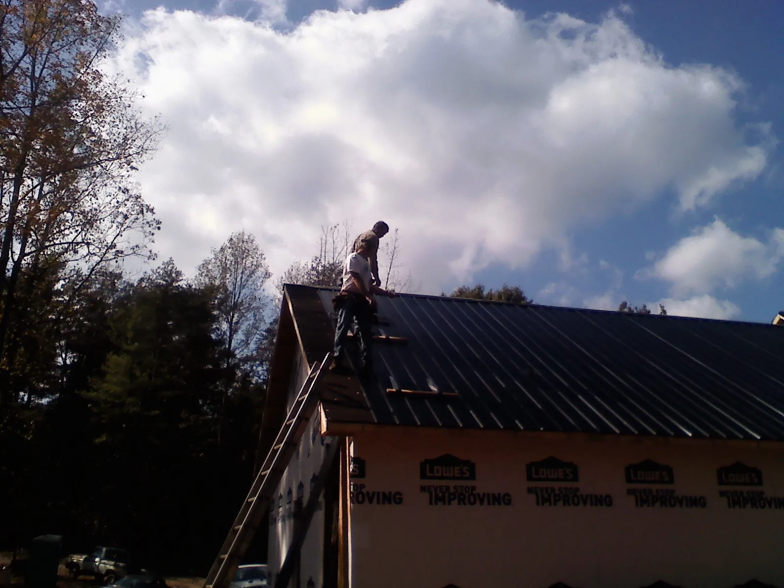 Roofer fastening dark metal panels high against a cloudy sky, from a Roof Inspection job in Autaugaville