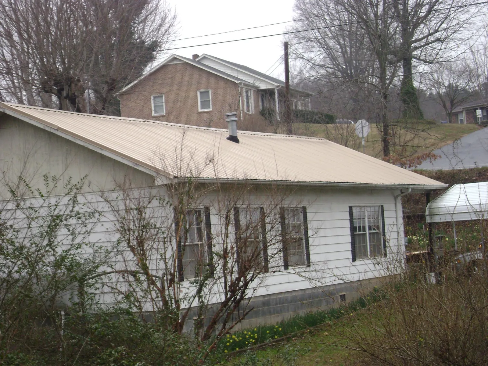 Tan metal roof on a white sided house set into a hillside — Commercial Roofing by Roofing Brothers in Autaugaville