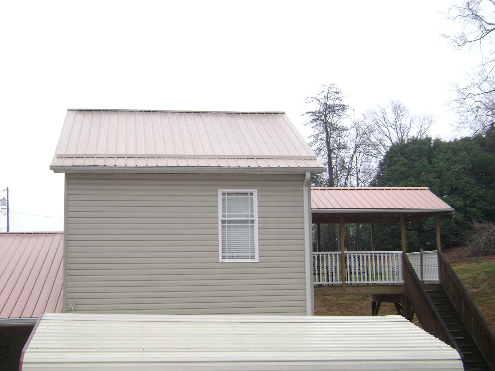 Tan metal roofs on a two story addition and attached porch, from a Roof Replacement job in Autaugaville